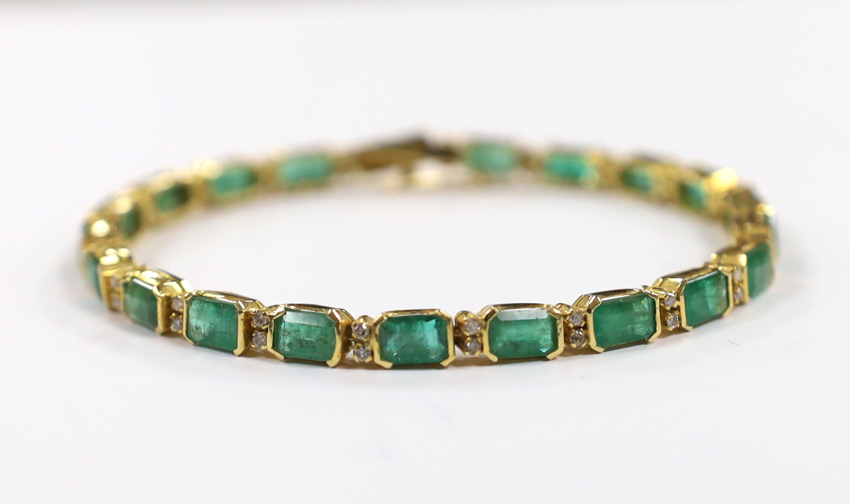 A modern 18k yellow metal and twenty stone emerald set line bracelet, with diamond chip spacers, 18cm, gross weight 13.5 grams.